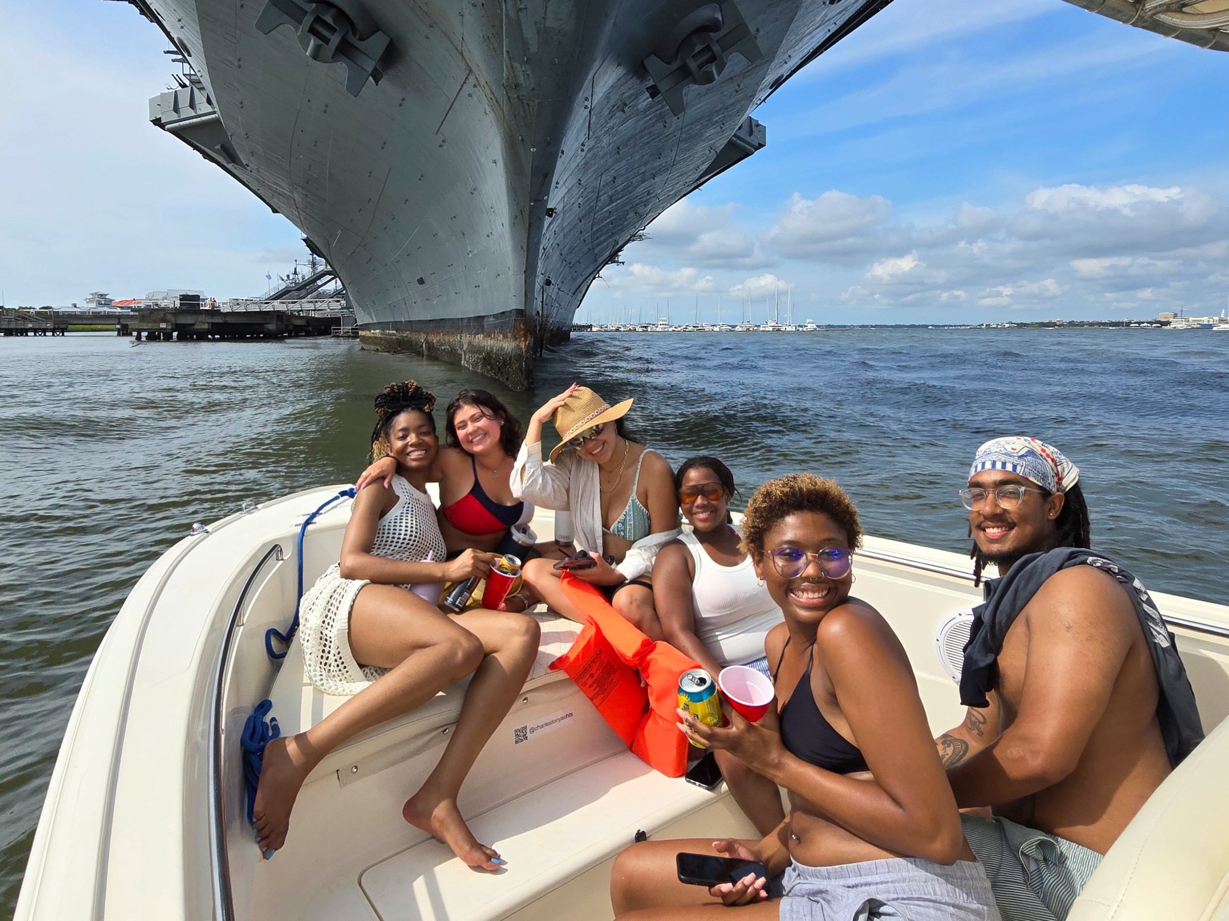 Group of friends smiling on a boat near a large ship under a sunny sky.