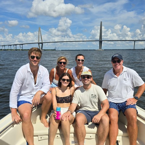Group of six people on a boat with a large suspension bridge in the background.