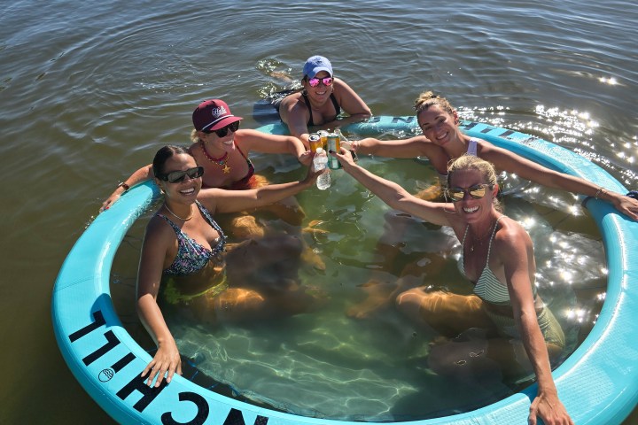 Five people in a circular float enjoying drinks in the water on a sunny day.