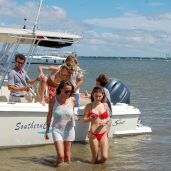 People on a boat by the shoreline, two women in swimsuits exiting the vessel.