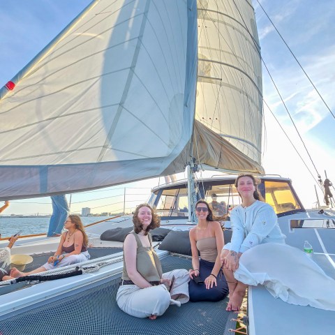 Group of people sitting on a sailboat deck with large sails on a sunny day.