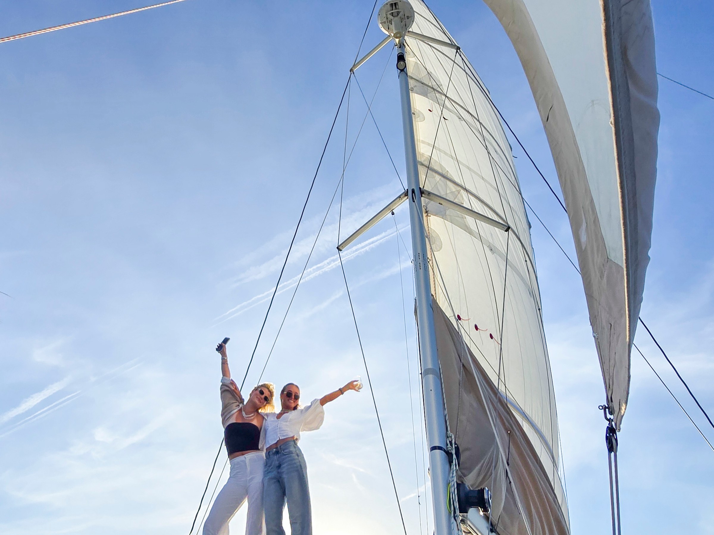 Two people standing on a yacht with sails up, enjoying the sunny day.