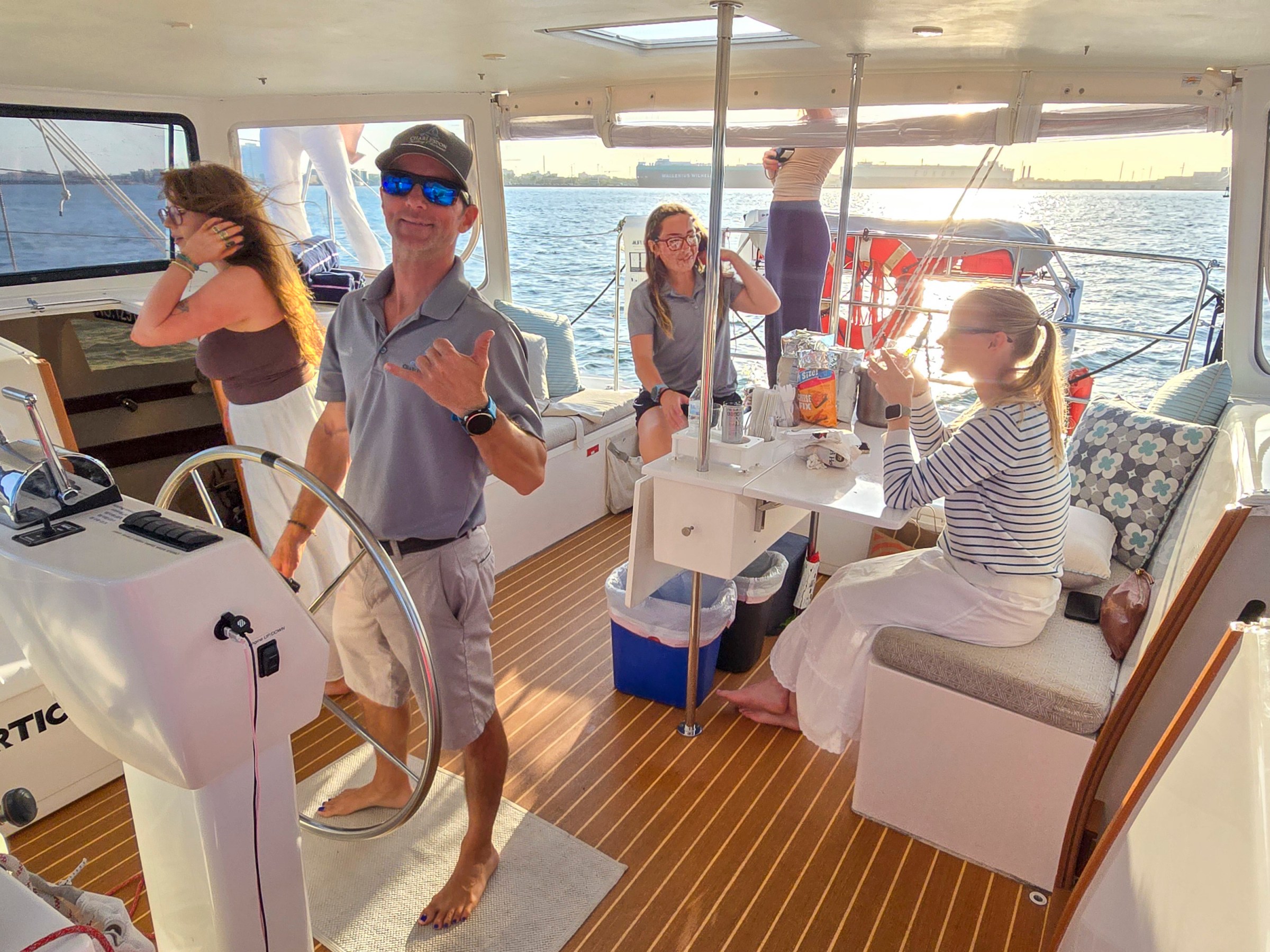 People on a boat enjoying a sunny day, one man posing with a hand gesture.