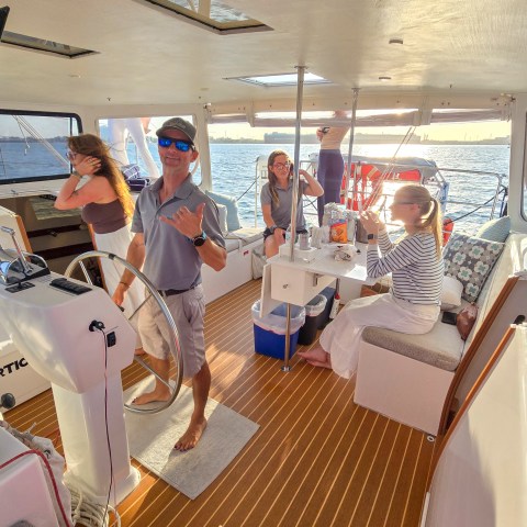 People on a boat enjoying a sunny day, one man posing with a hand gesture.