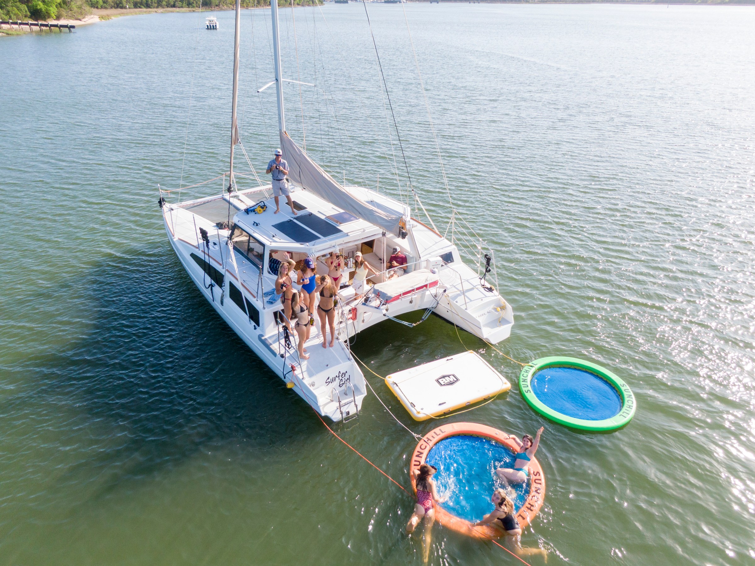 People on a catamaran in the water with inflatable floats nearby.