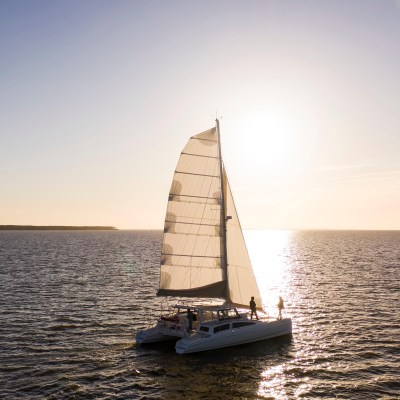 Sailboat on calm water at sunset with clear sky and bright sun.