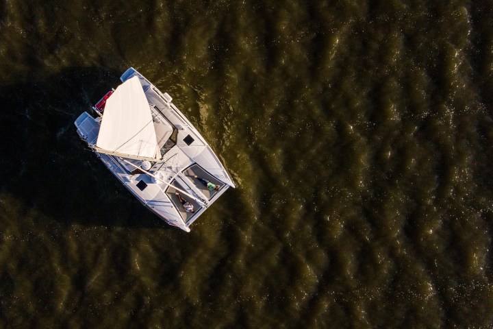 Aerial view of a sailboat on dark water with sails set.