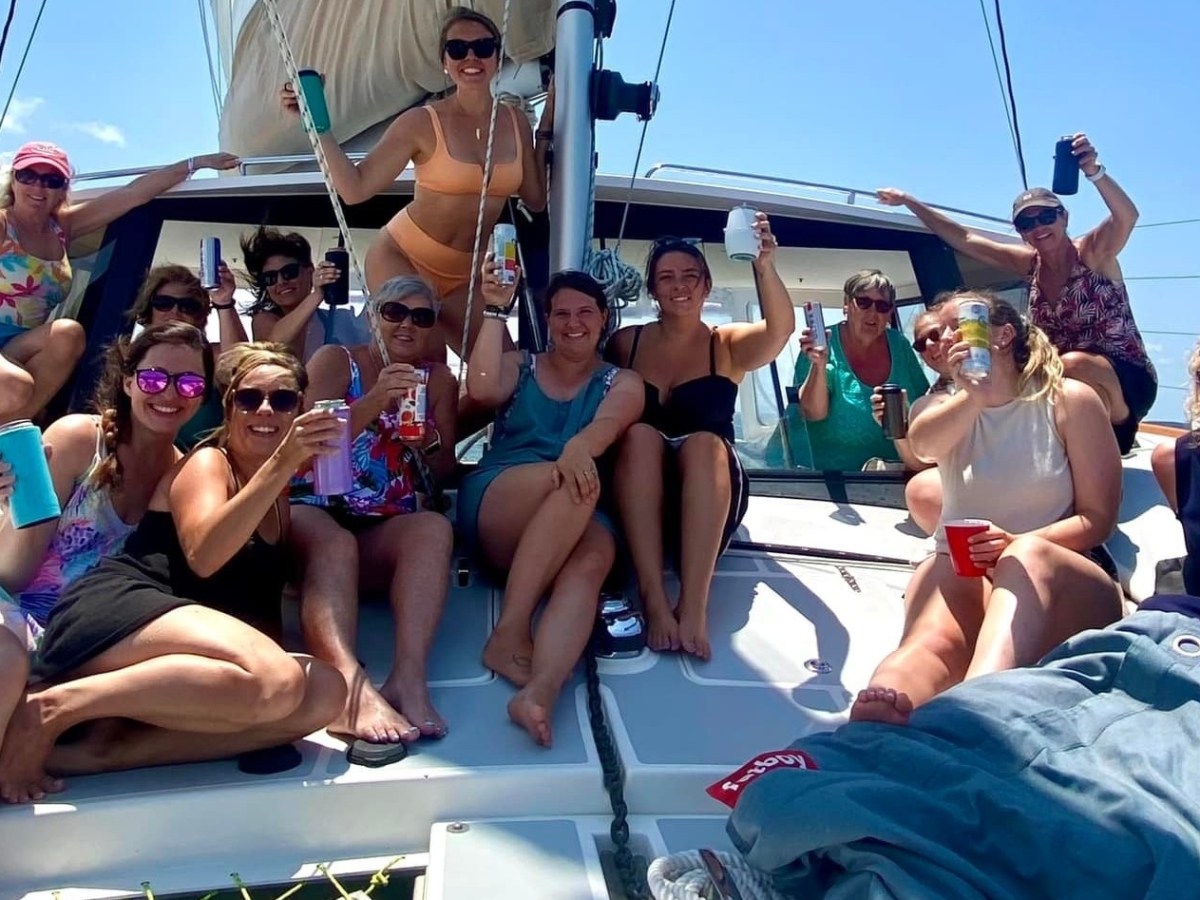 Group of women on a boat deck enjoying drinks and sunshine under a clear blue sky.