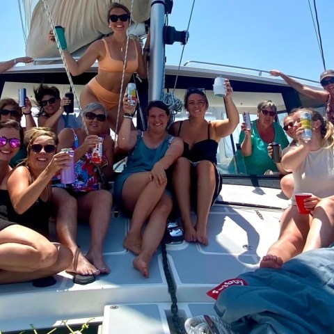 Group of women on a boat deck enjoying drinks and sunshine under a clear blue sky.