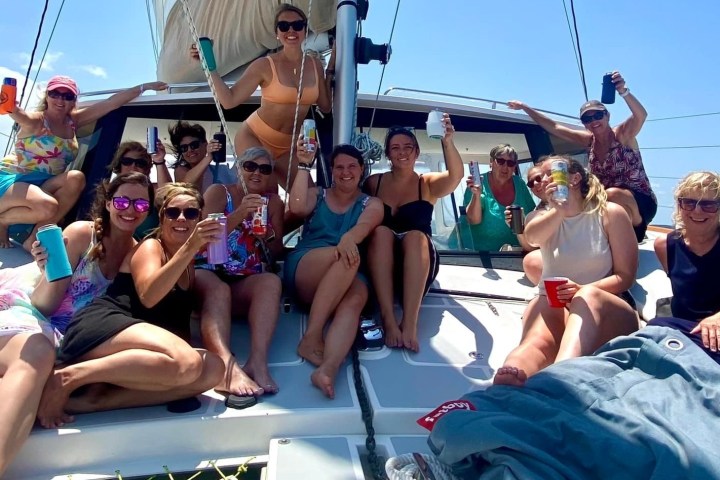 Group of women on a boat deck enjoying drinks and sunshine under a clear blue sky.