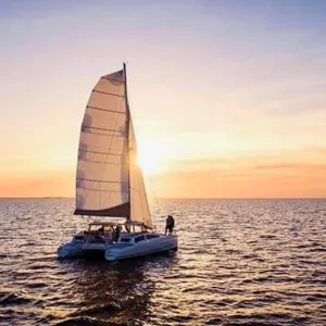Sailboat on calm ocean at sunset with sun shining through the sail.