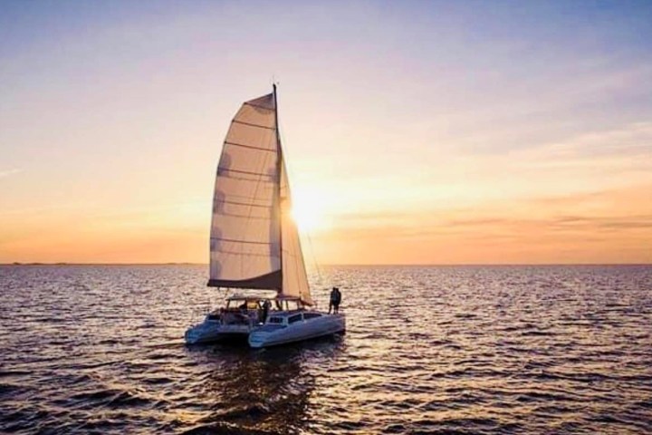 Sailboat on calm ocean at sunset with sun shining through the sail.