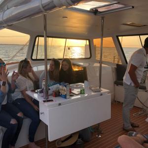 Group of people socializing on a boat during sunset, with snacks and drinks on the table.