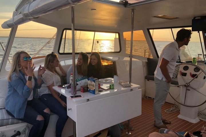 Group of people socializing on a boat during sunset, with snacks and drinks on the table.