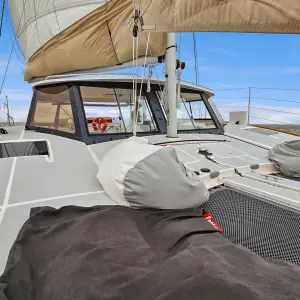 View of a boat deck with sails, lifebuoy, and sea in the background under a clear blue sky.