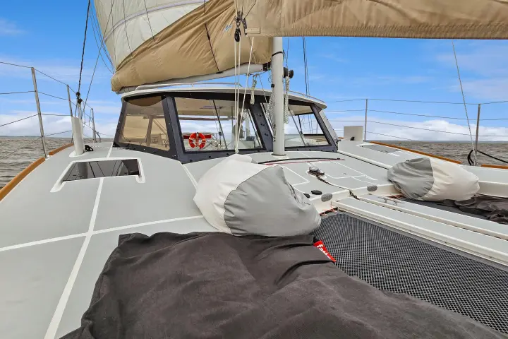 View of a boat deck with sails, lifebuoy, and sea in the background under a clear blue sky.
