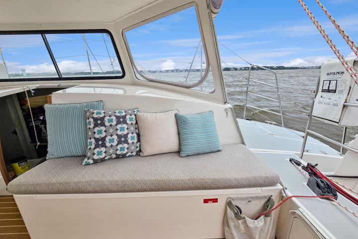Boat interior with cushioned seating, decorative pillows, and view of water through windows.