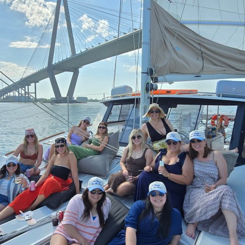Group of women on a boat near a suspension bridge on a sunny day.