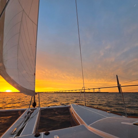 Sailboat at sunset with bridge in the background on open water.