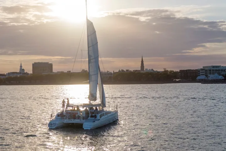 Sunset over water with a sailboat, buildings visible in the background.