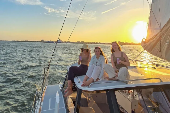 Three people on a sailboat enjoy sunset views over the water.