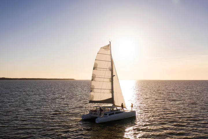 Sailboat on calm water at sunset, with sunlit sail and clear sky.