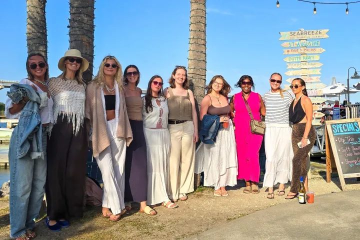 Group of women posing by palm trees and waterfront dock.