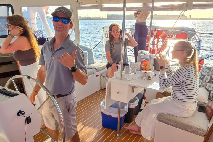Four people relaxing on a boat at sunset, with one steering and others seated.